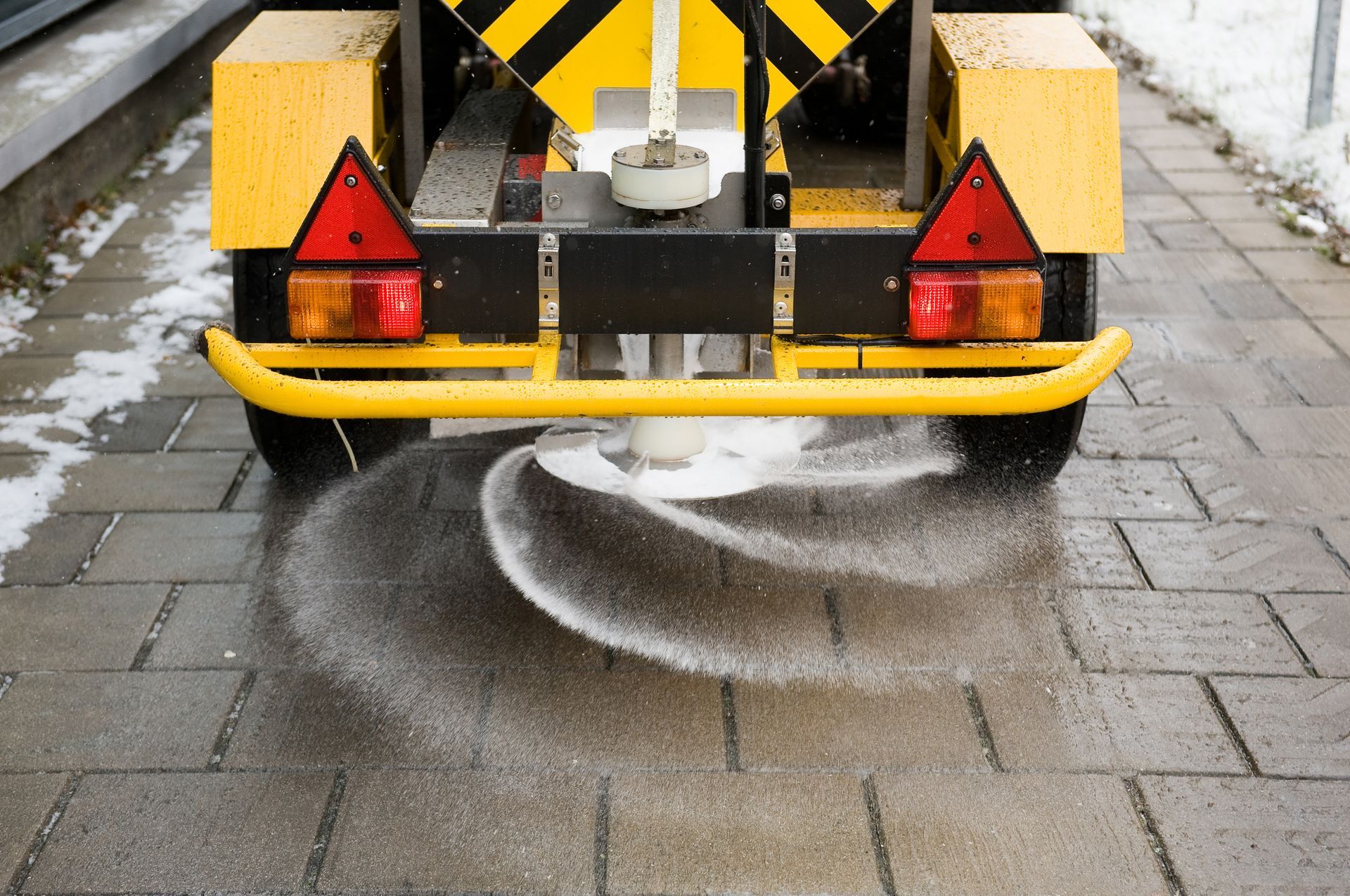 A yellow and black vehicle is spreading salt on a sidewalk