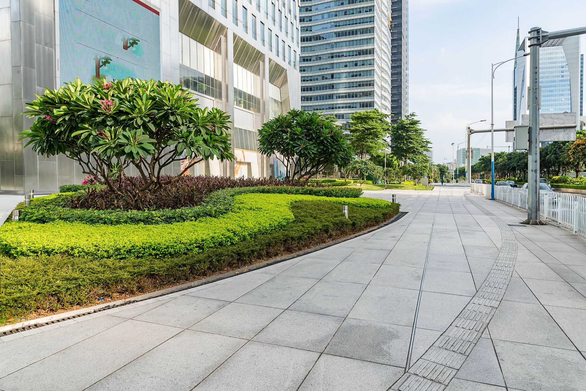 An empty sidewalk in front of a building with trees and bushes.