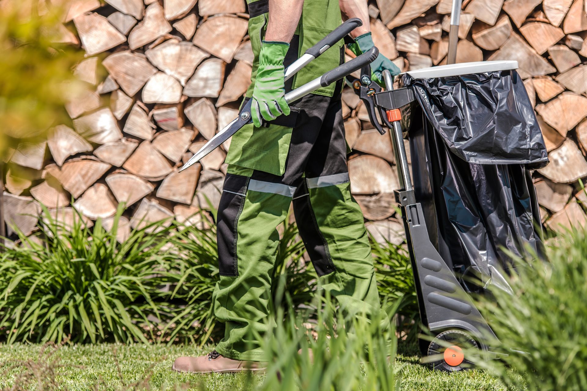 A man is standing in a garden holding a rake and a trash can.