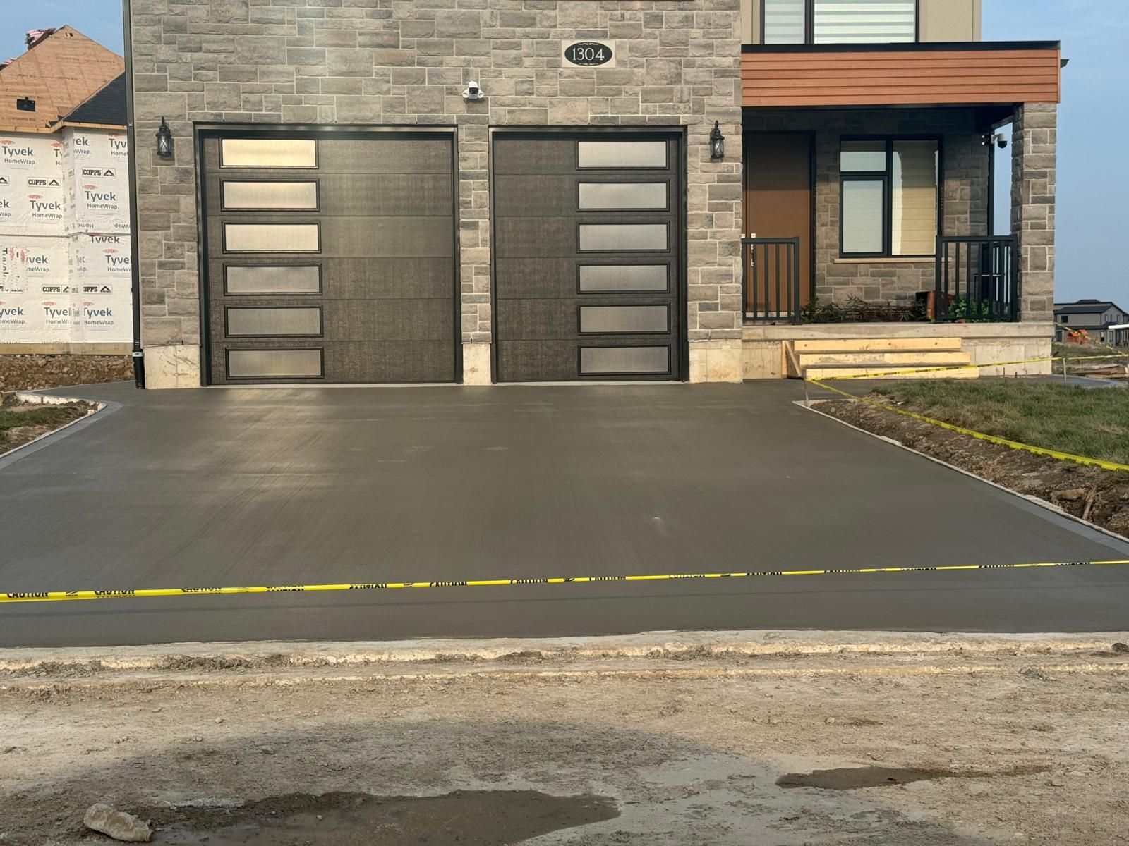 New concrete driveway in front of a modern house with two garage doors and stone facade.