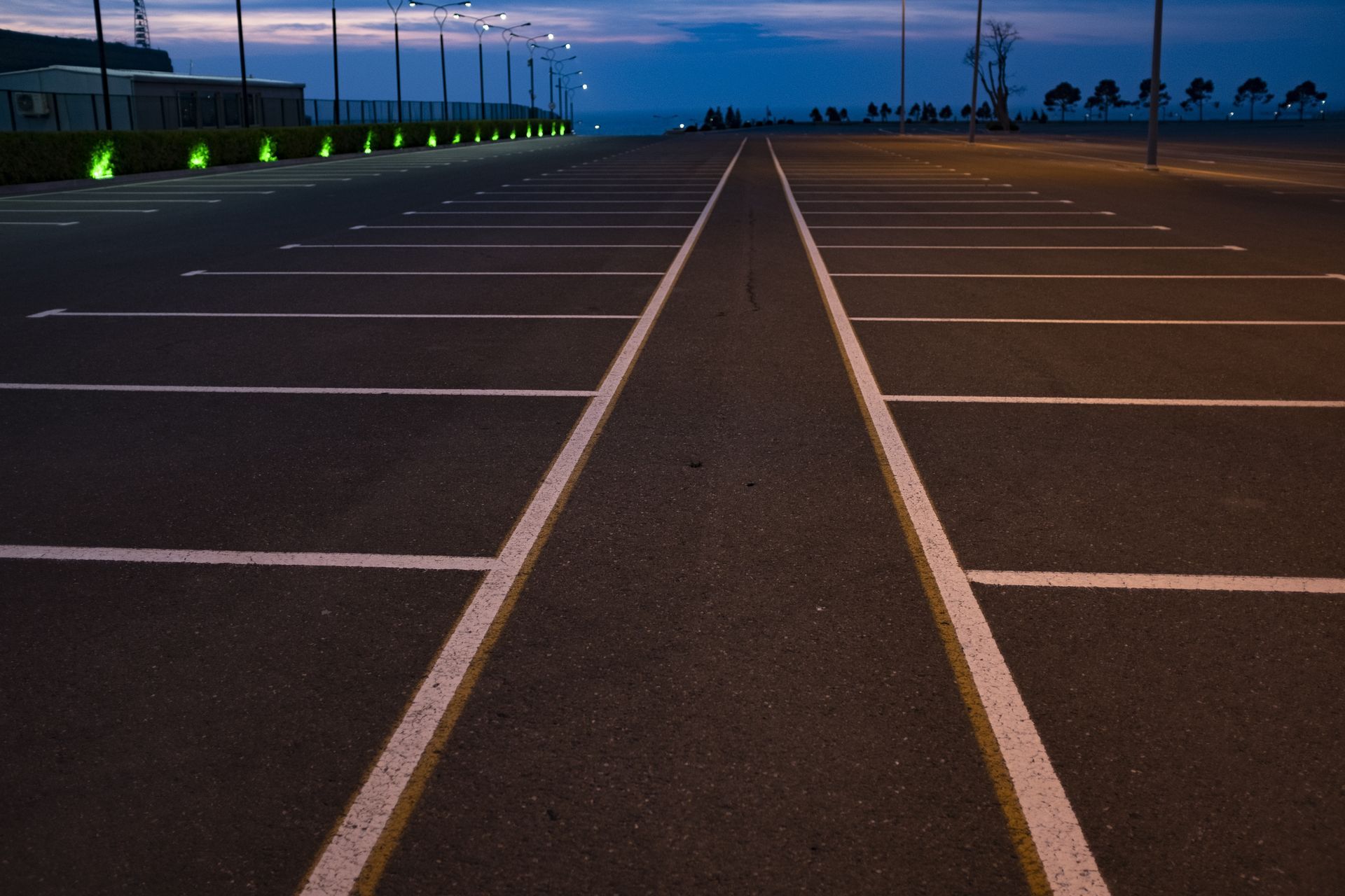 Empty parking lot at dusk with white-lined spaces and a dark central lane