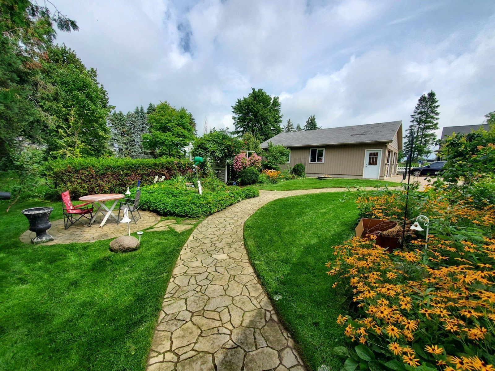 Stone path through a lush garden leads to a one-story building under a cloudy sky.