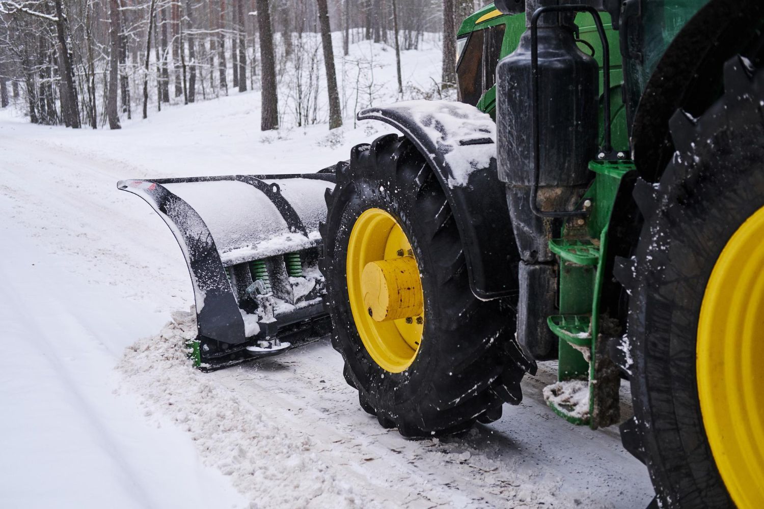 Snowplow on a John Deere tractor clearing a snow-covered road, outdoors.