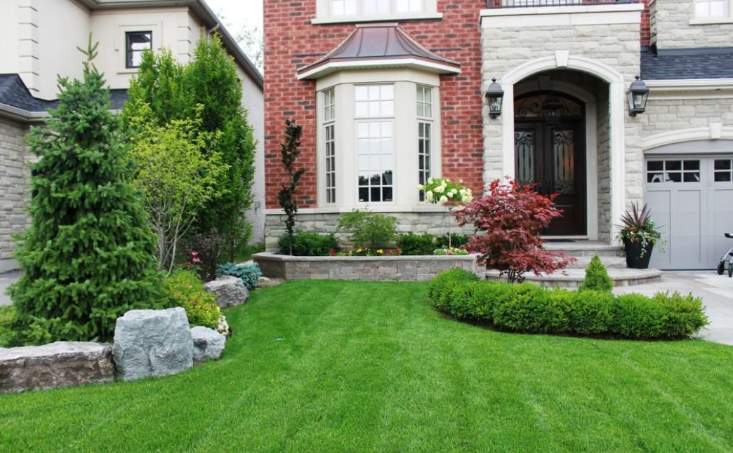 Front yard with manicured lawn, shrubs, and a brick-and-stone house facade with an arched entryway