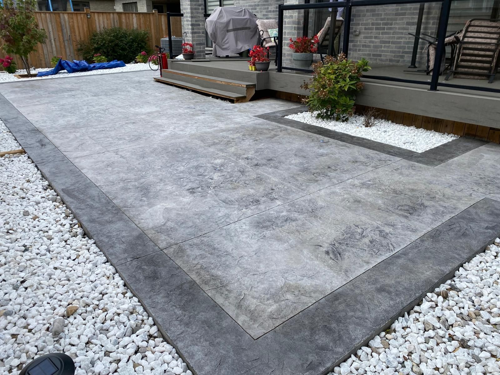 A concrete patio with a black border and white gravel in front of a house.