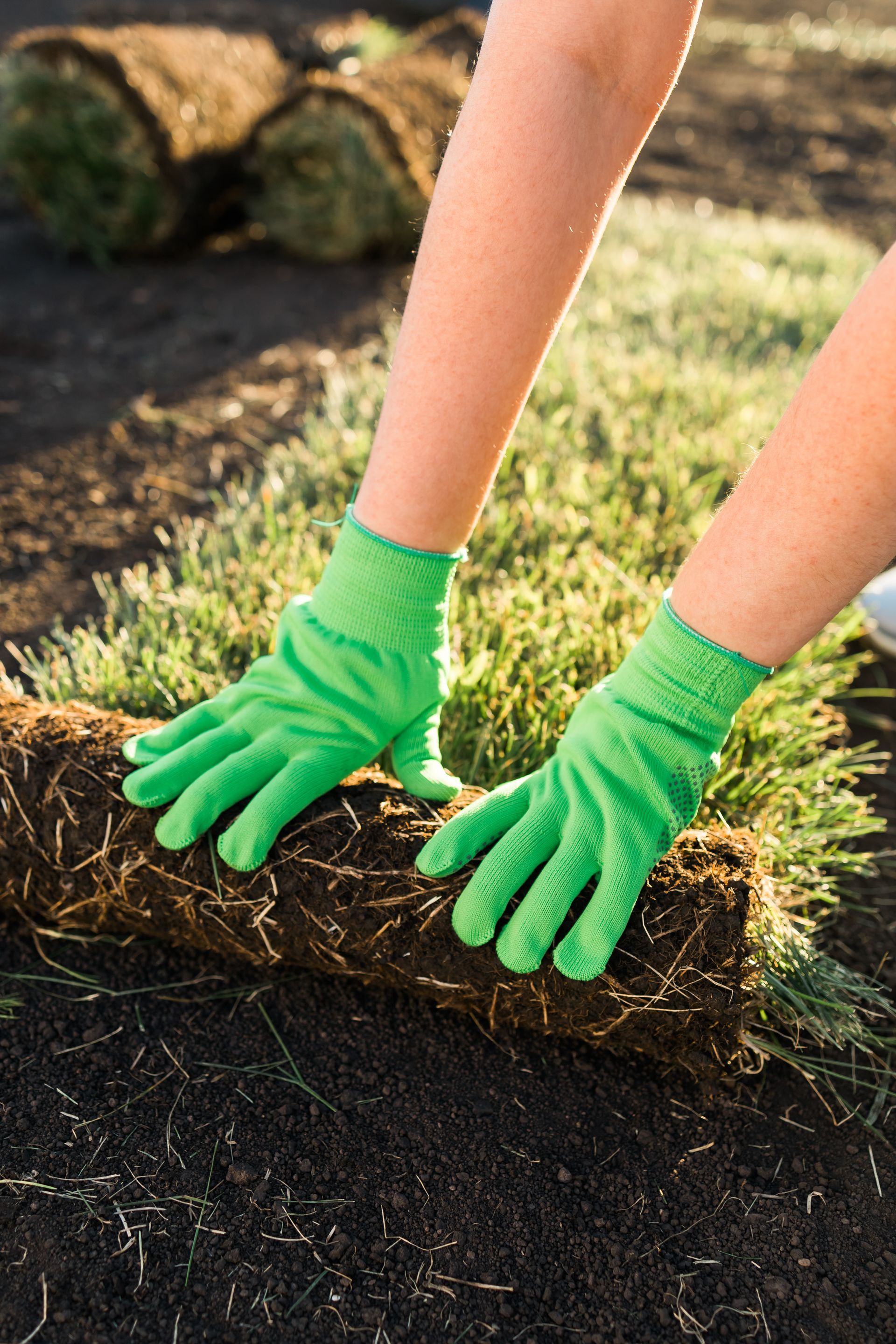 A person wearing green gloves is rolling a roll of grass.
