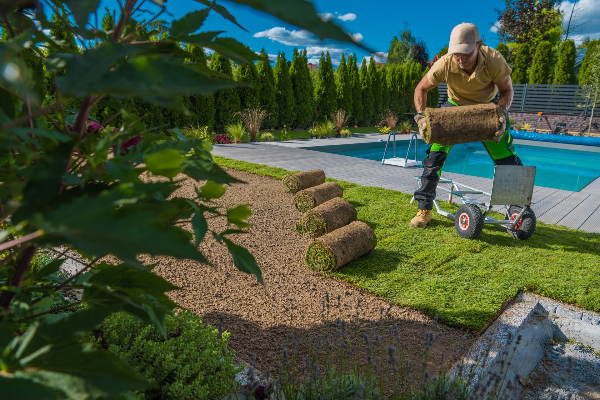 A man is rolling rolls of turf in a backyard next to a pool.