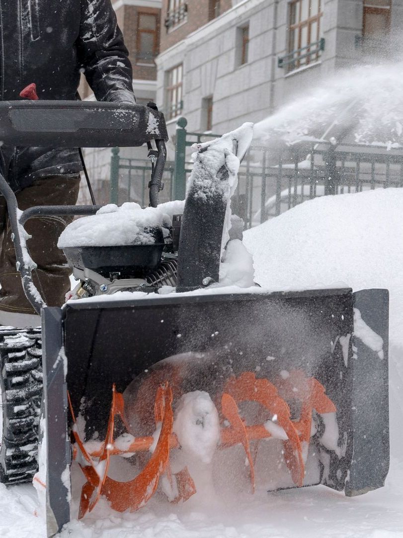 A man is using a snow blower to clear snow from a sidewalk.