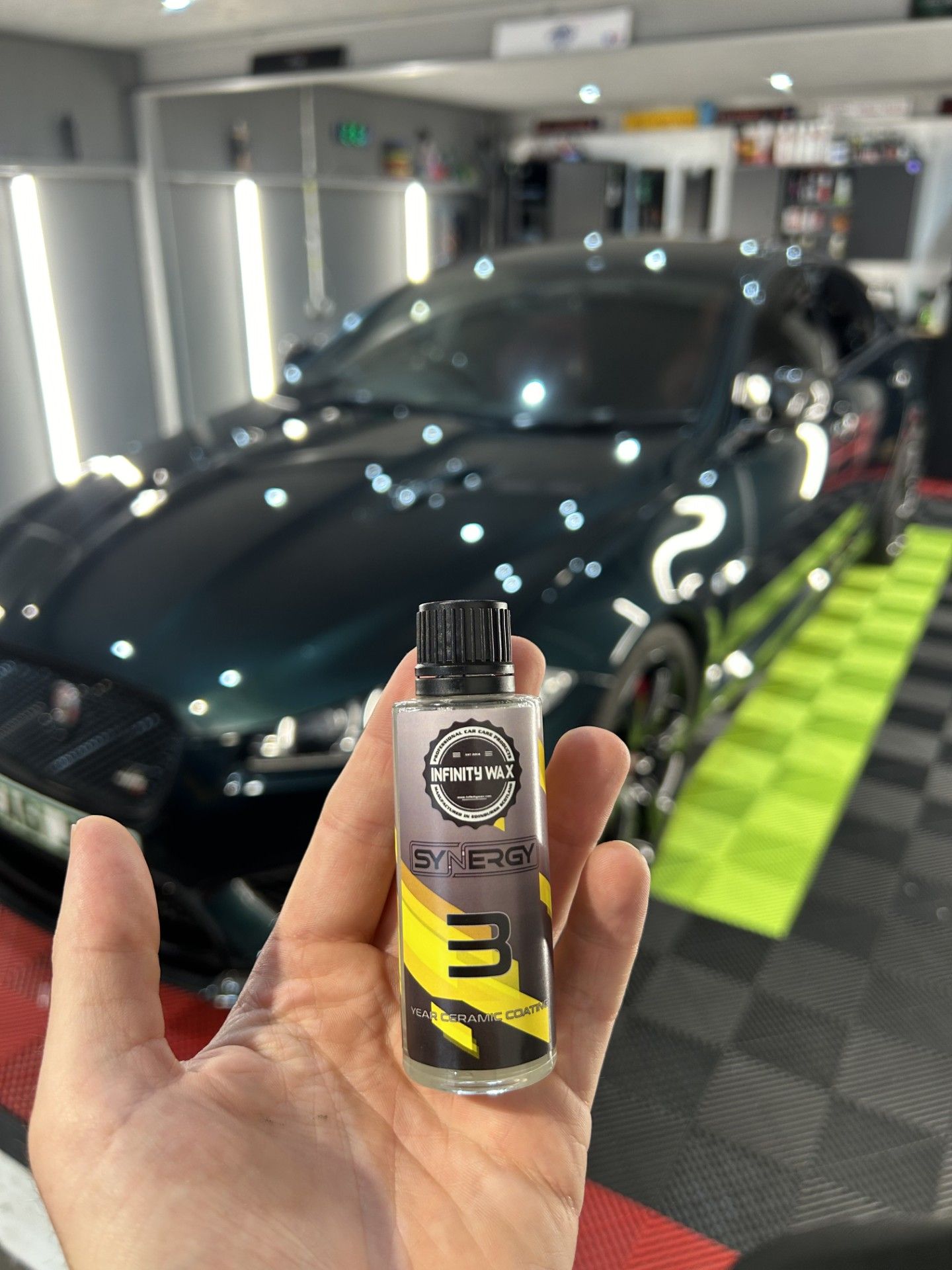 A person is holding a small bottle in front of a car.