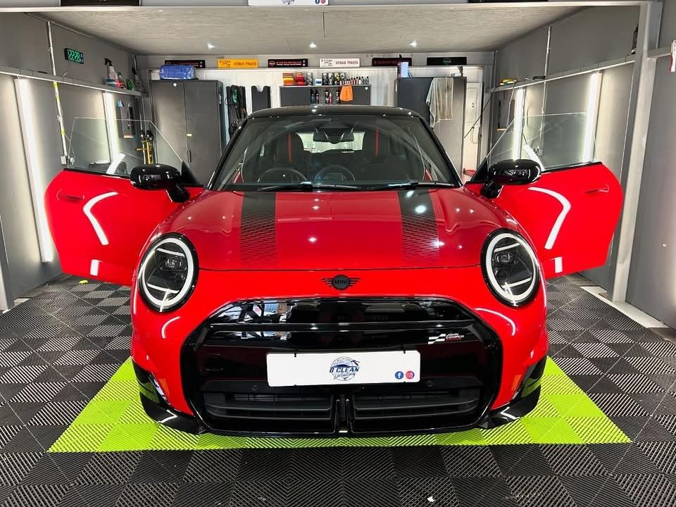 A red mini cooper is parked in a garage with its doors open.