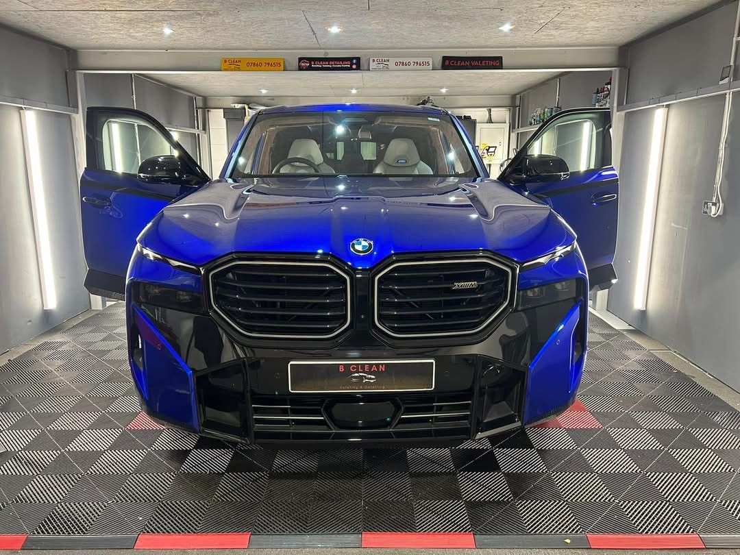 A blue bmw is parked in a garage with its doors open.