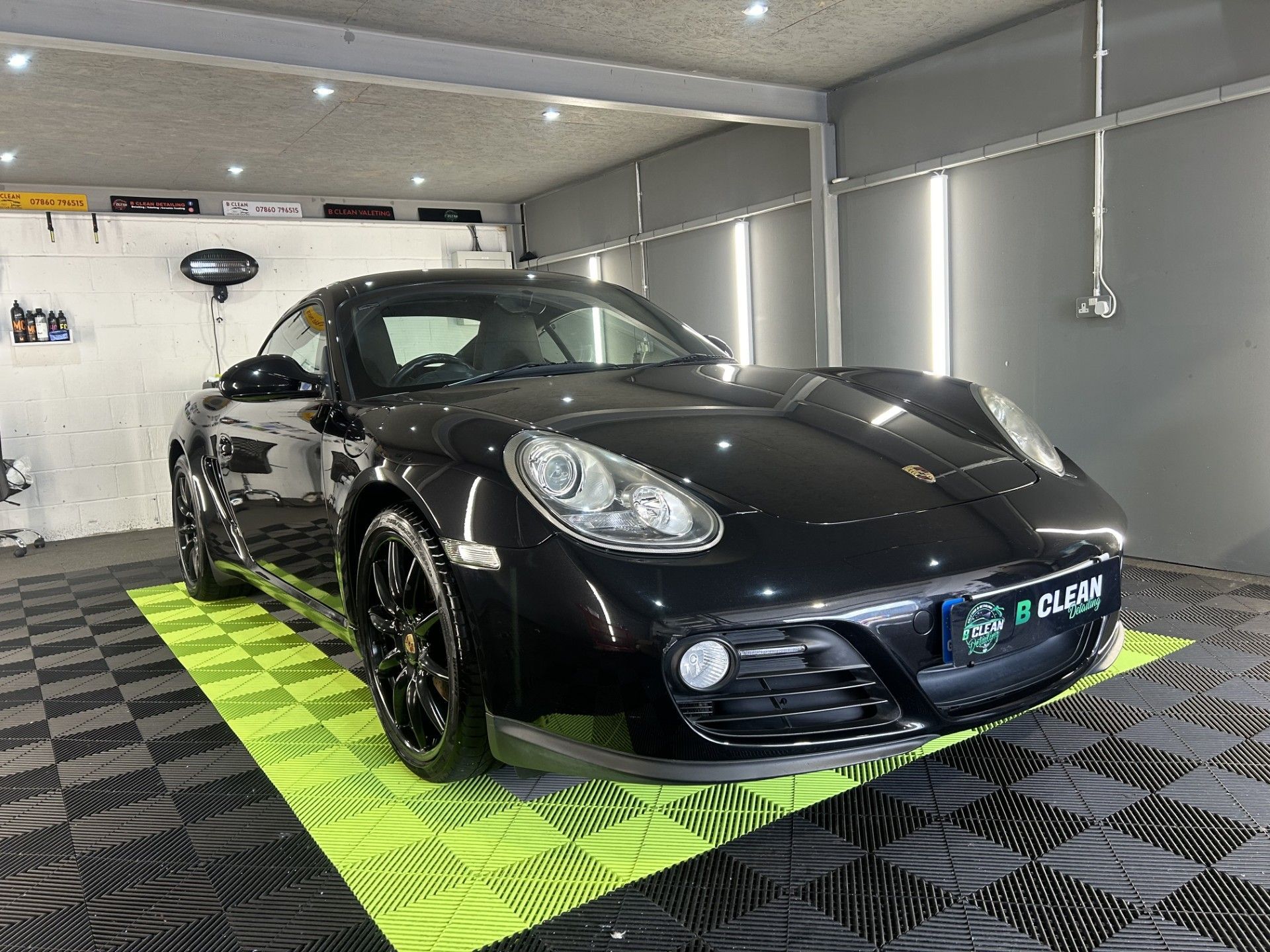A black porsche boxster is sitting on a yellow mat in a garage.
