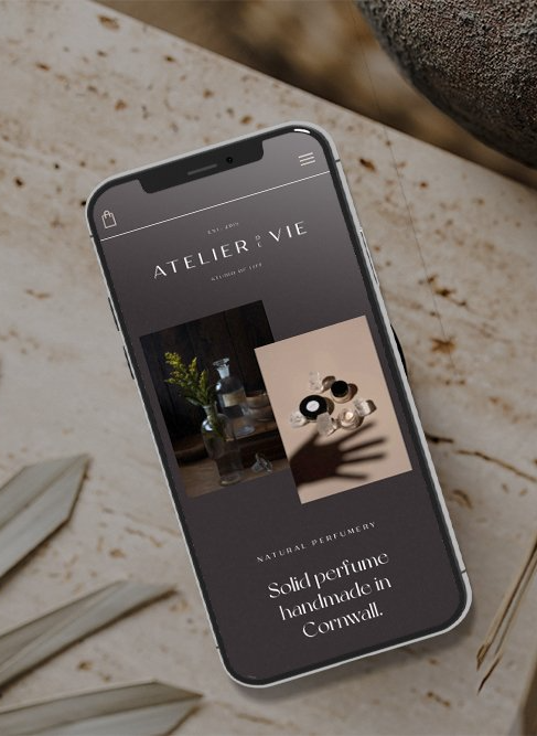 Smartphone displaying the Atelier de Vie website, featuring product photos and text on a textured surface.