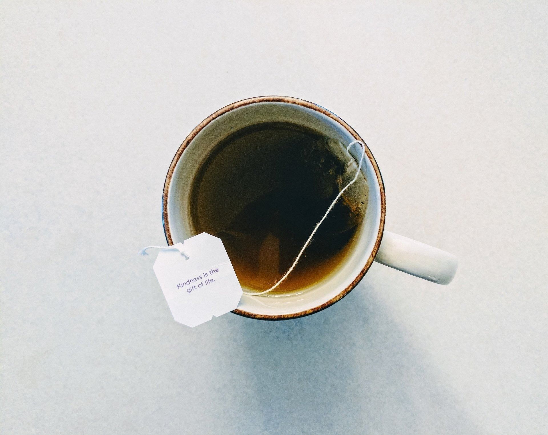 Cup of tea with a tea bag; white mug on a white surface.