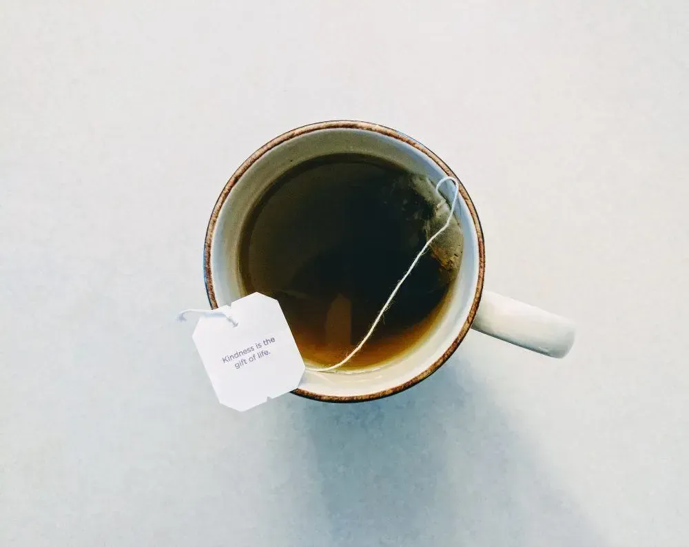 Mug of tea with a teabag. White mug on a white surface, tea is brown. Teabag label reads 