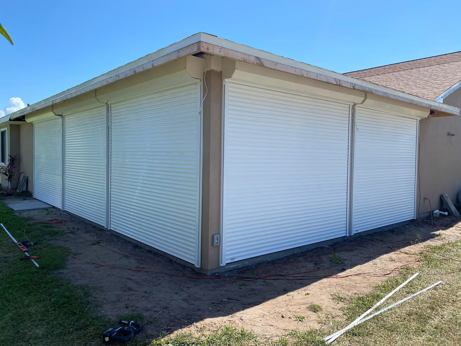 White roll-down shutters enclose a covered patio; beige trim; bright blue sky in background.