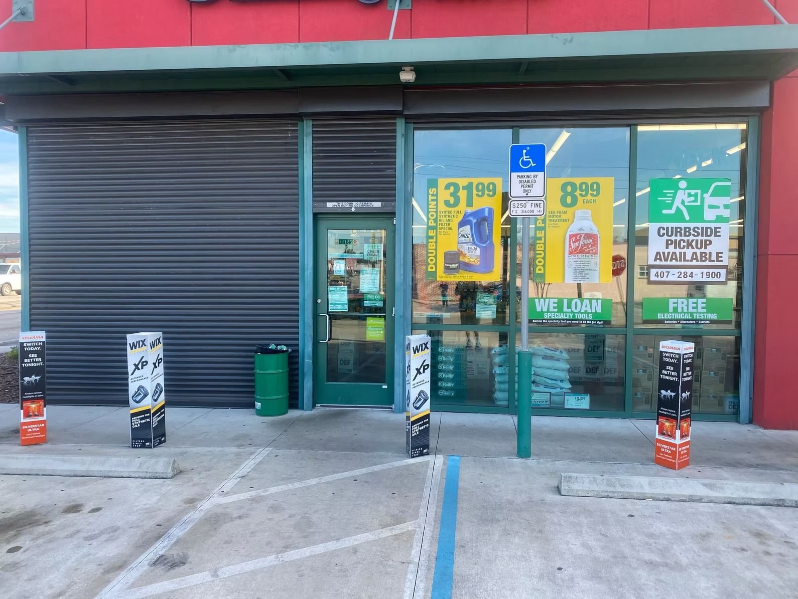 Convenience store exterior with closed security shutter, glass windows displaying products, accessible parking sign.