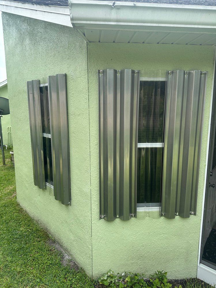 Green house corner with corrugated metal hurricane shutters protecting windows.