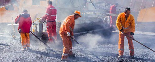 Construction workers smoothing out asphalt on roadway