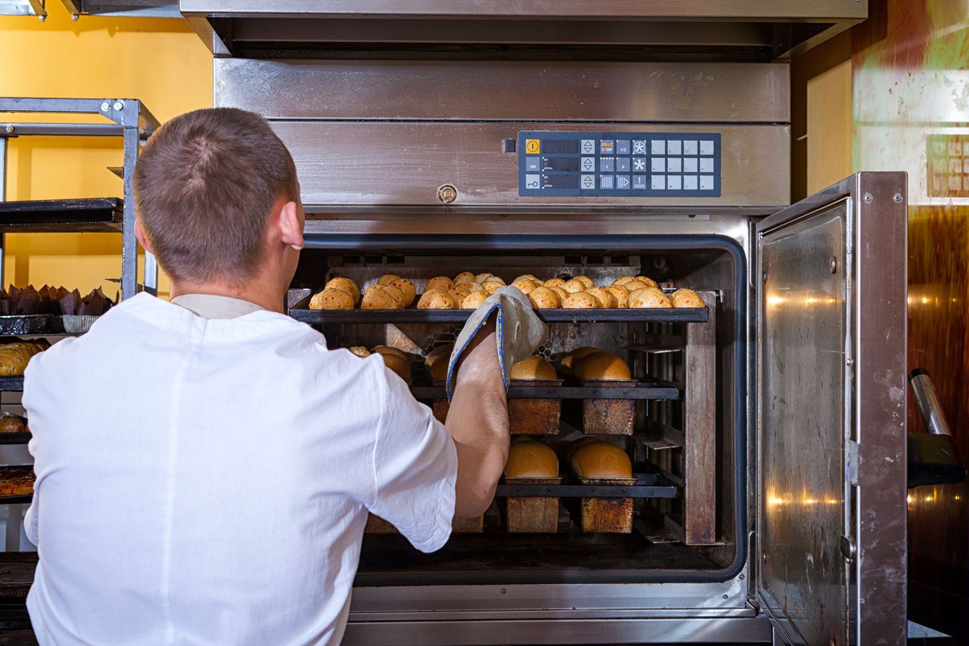 A man removing baked goods from a commercial oven.
