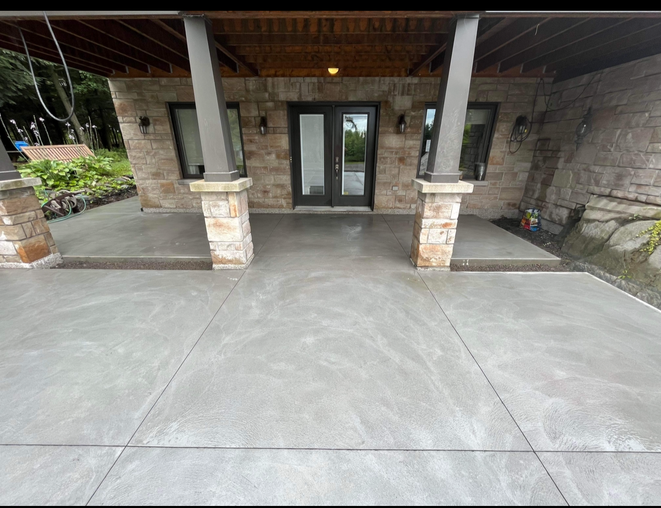 Un patio en béton devant une maison en brique avec un porche couvert.