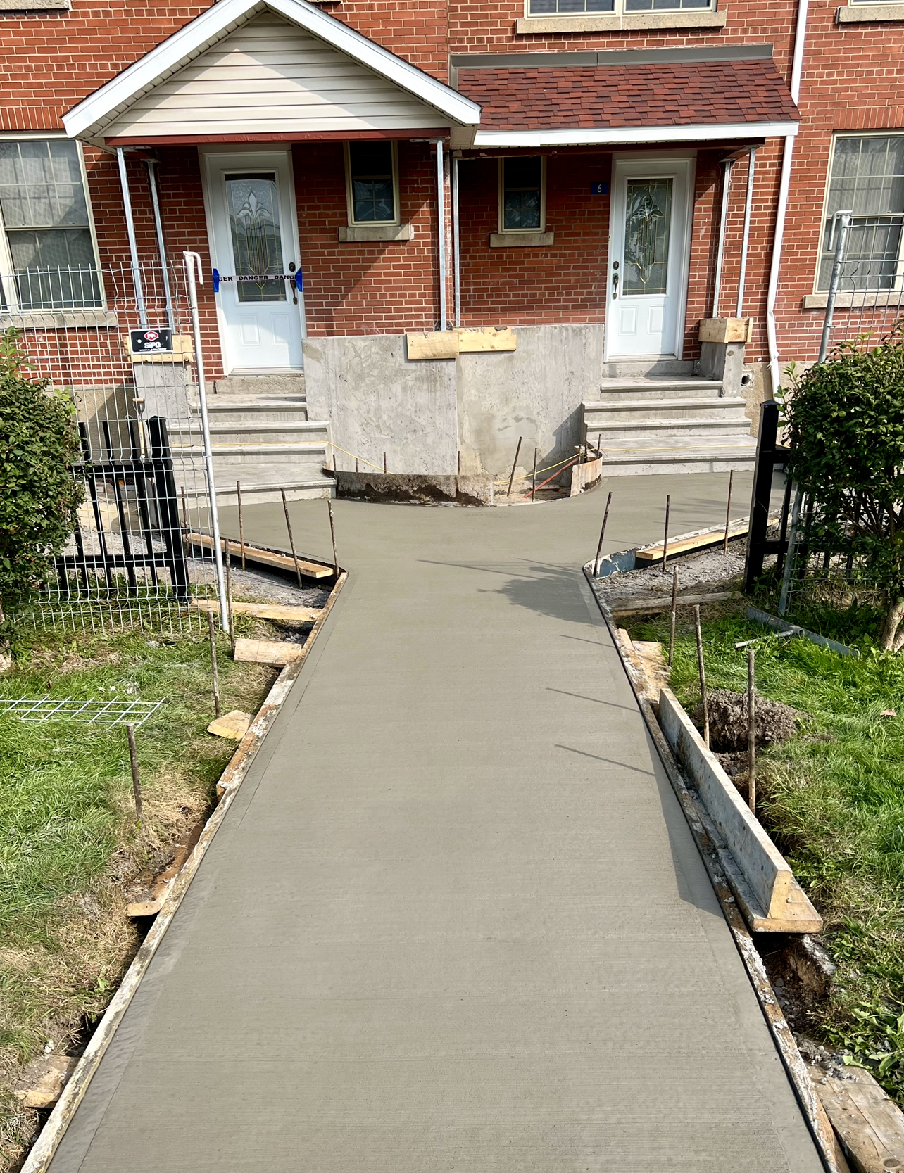 Une passerelle en béton est en cours de construction devant une maison en brique.