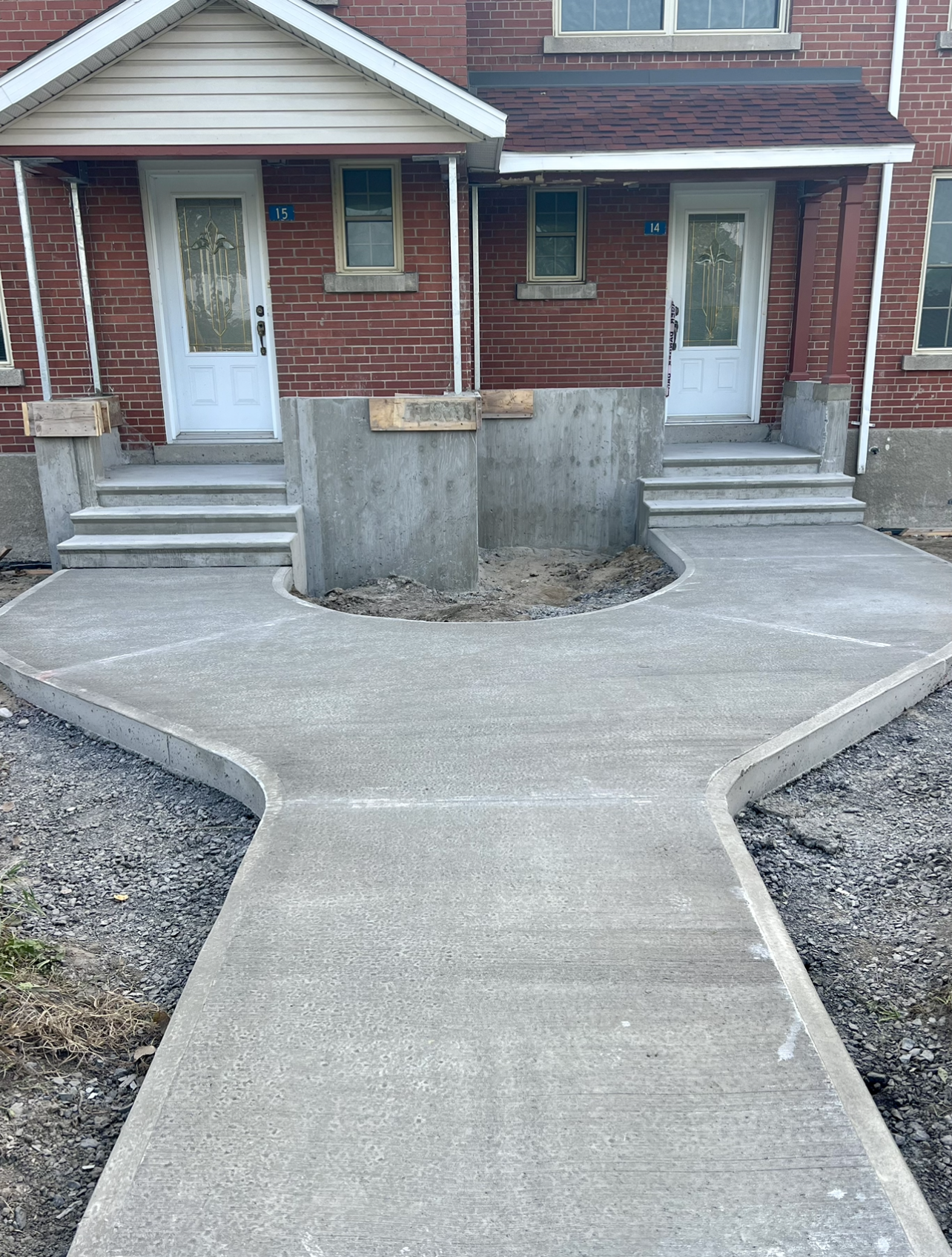 Une passerelle en béton est en cours de construction devant une maison en brique.