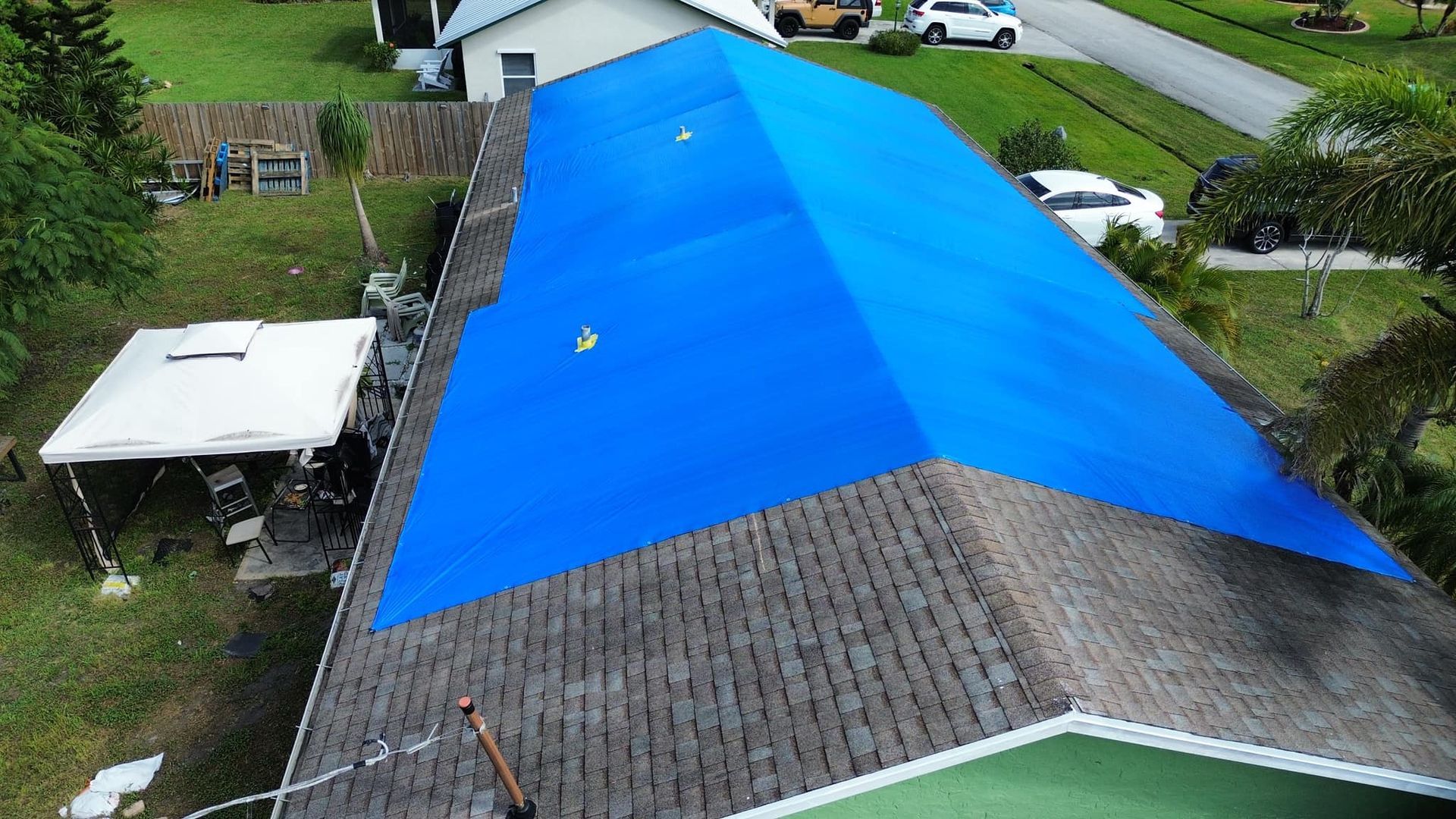 An aerial view of a house with a blue tarp on the roof
