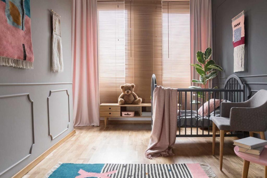 A baby room with a crib , chair , rug and paintings on the wall.