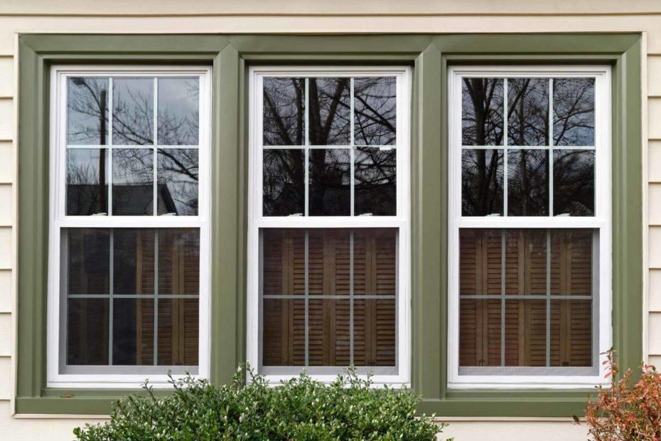 Three windows on the side of a house with green trim.