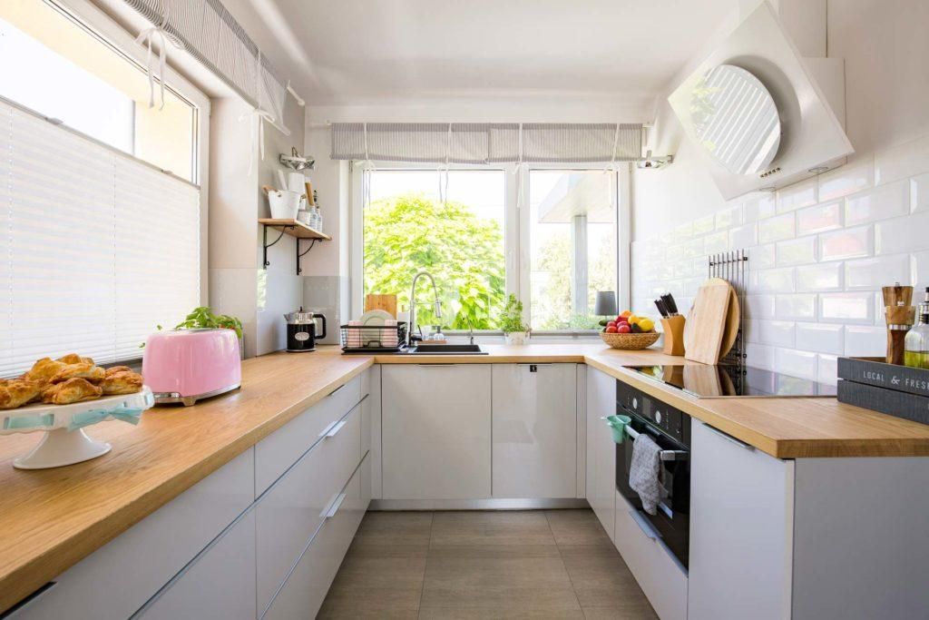 A kitchen with white cabinets , wooden counter tops , a stove and a window.