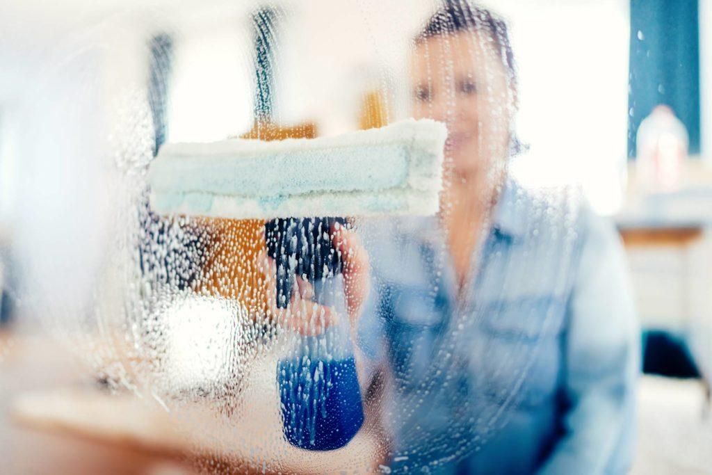 A woman is cleaning a window with a spray bottle.