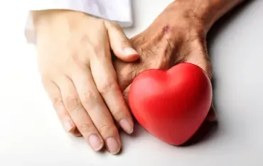 Young hand holding an older hand and a red heart, symbolizing care.