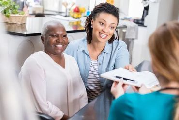Woman with daughter reviewing paperwork with a professional in a home kitchen.