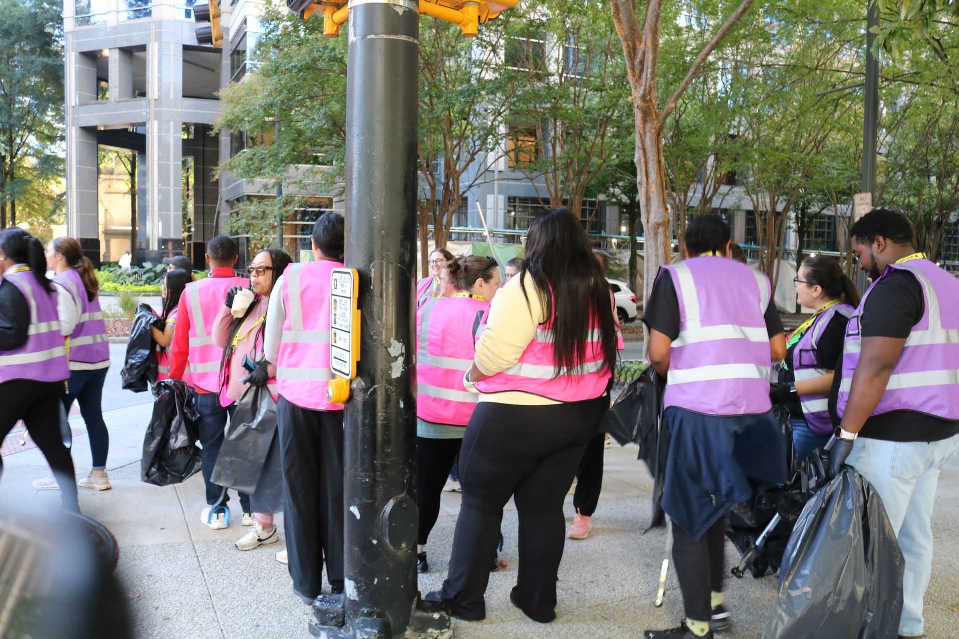 People in pink vests cleaning up debris on a sidewalk near buildings and trees.