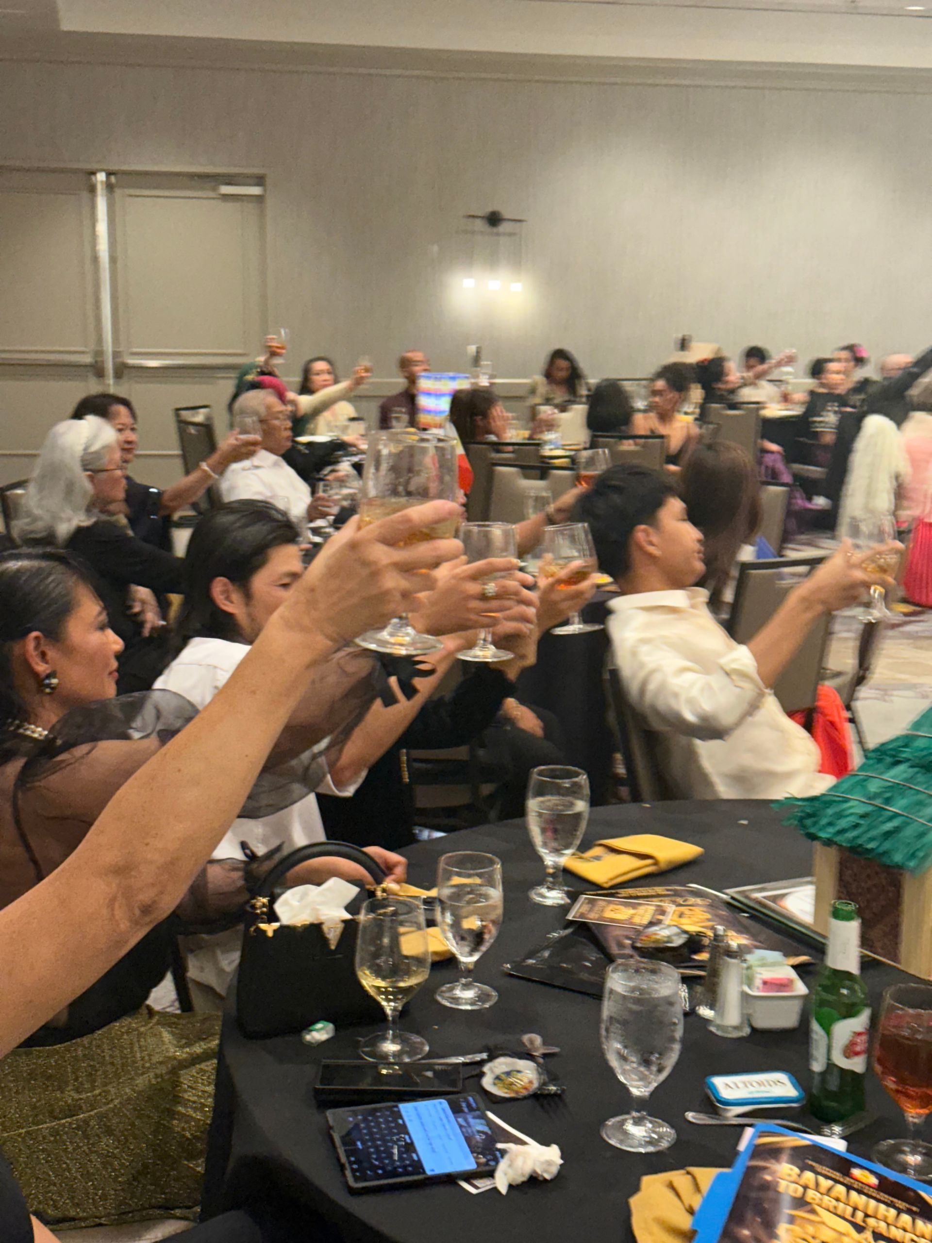 People at tables in a banquet hall raise glasses in a toast.