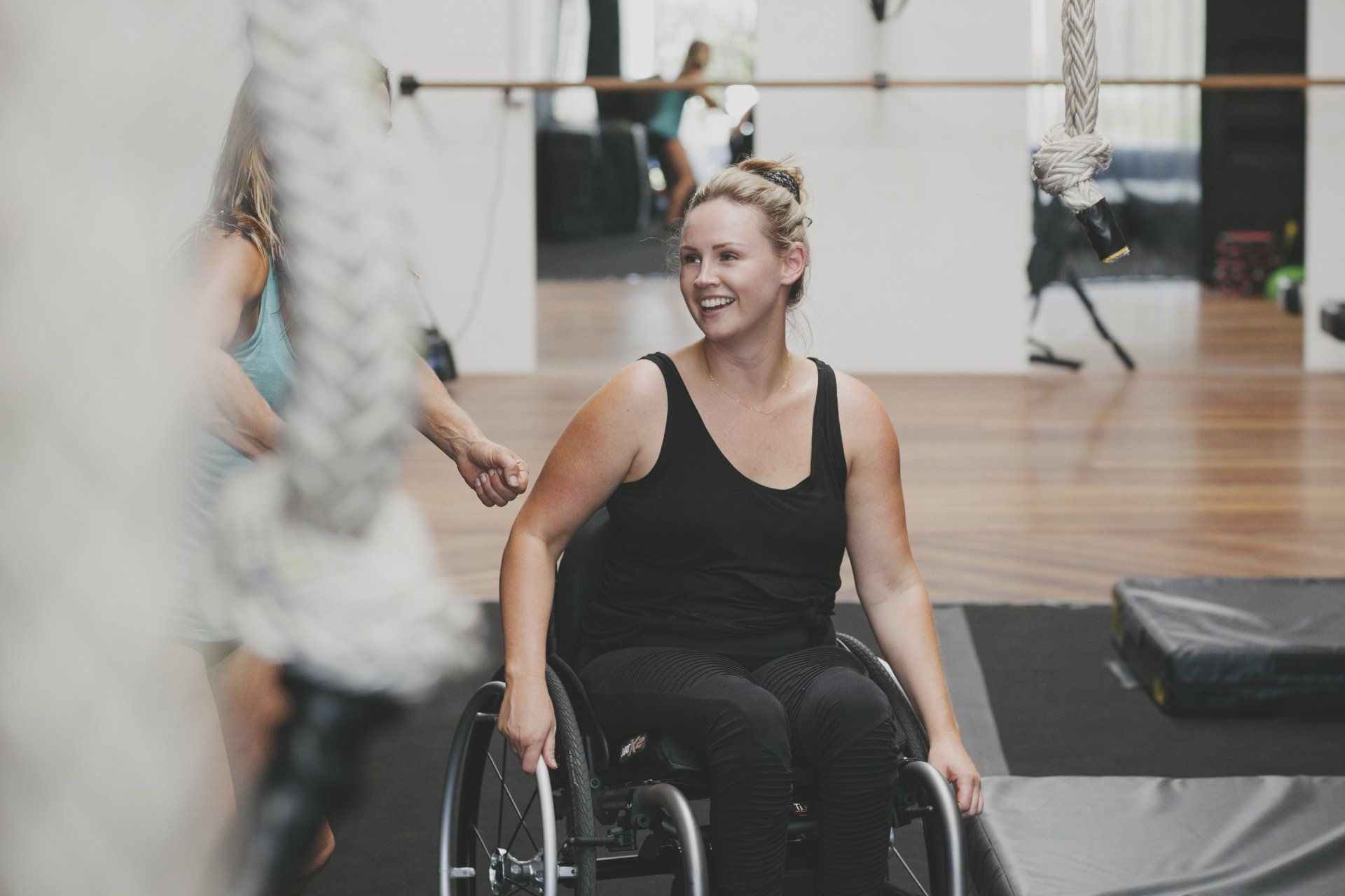 Woman in wheelchair smiles during exercise in a gym.