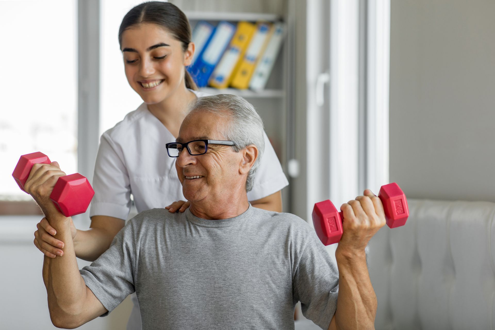 Woman assisting elderly man with lifting weights in a home setting. Both smiling.