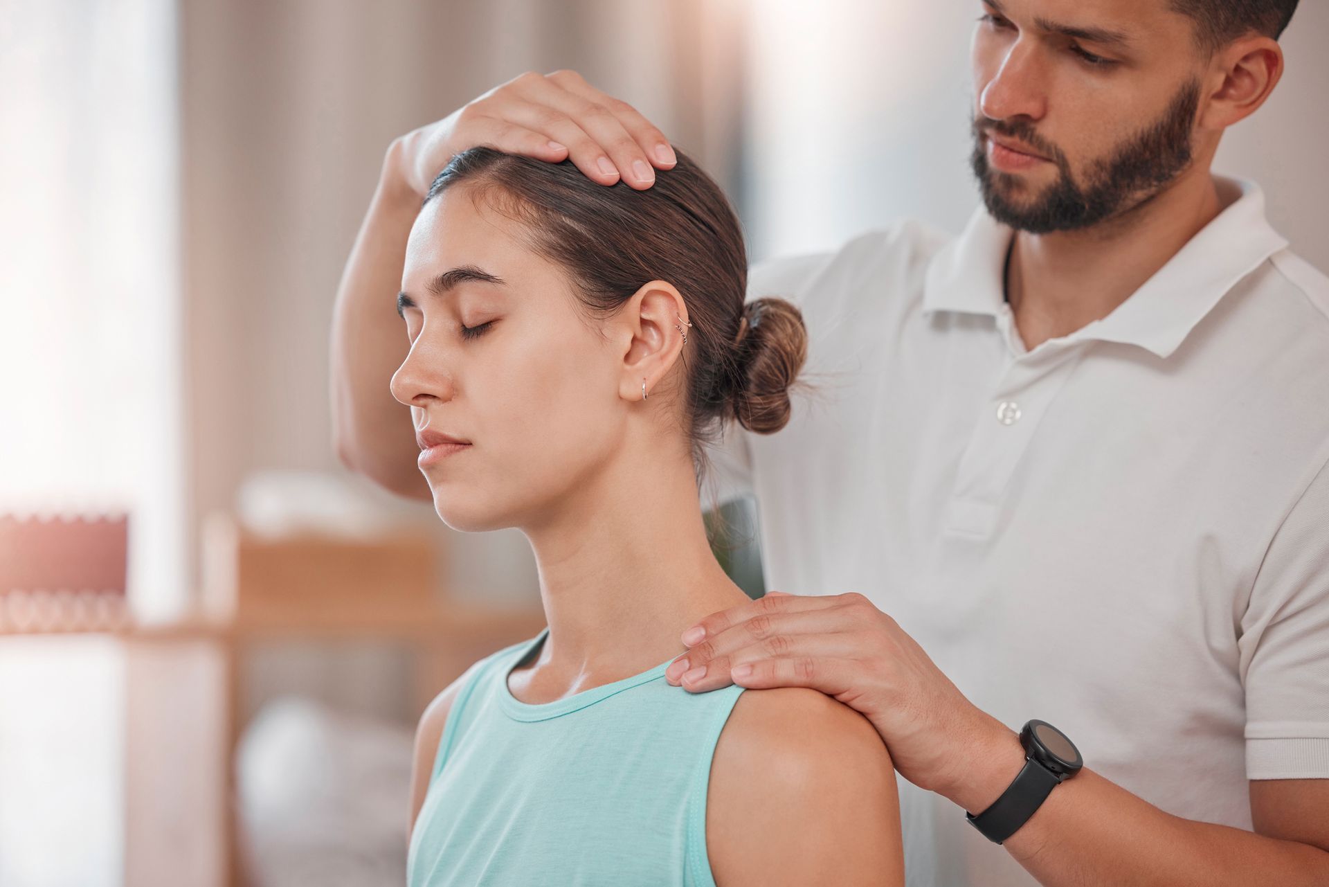 Man performing a neck and shoulder examination on a woman in a bright room.