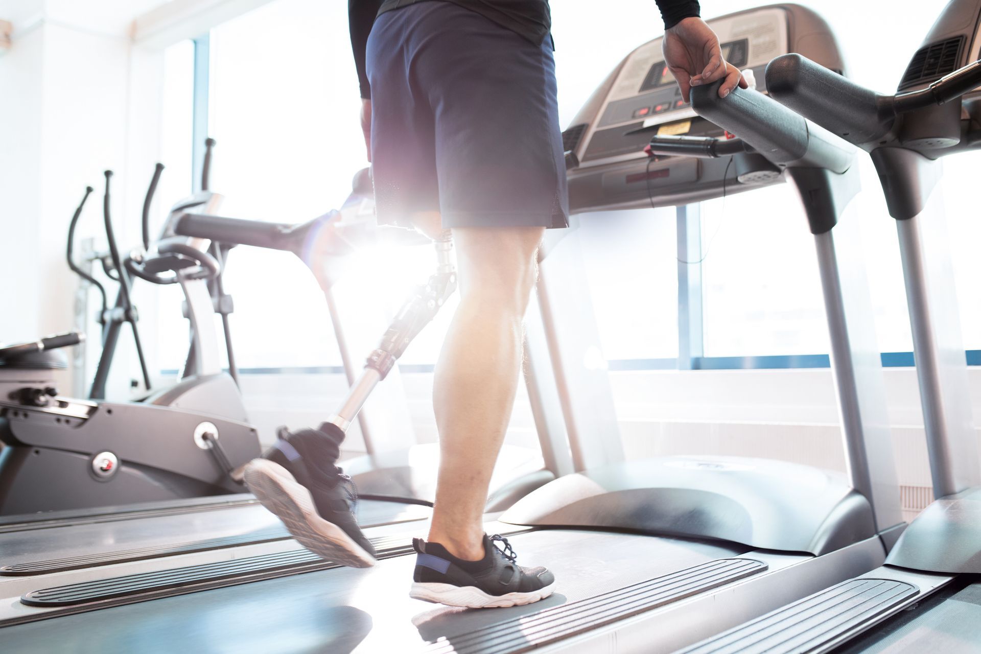 Man with prosthetic leg walking on a treadmill in a gym.