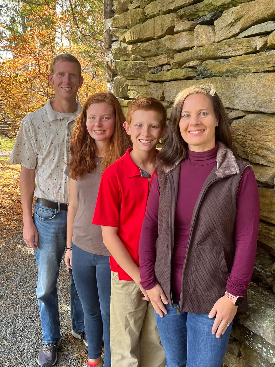 A family is posing for a picture in front of a stone wall.