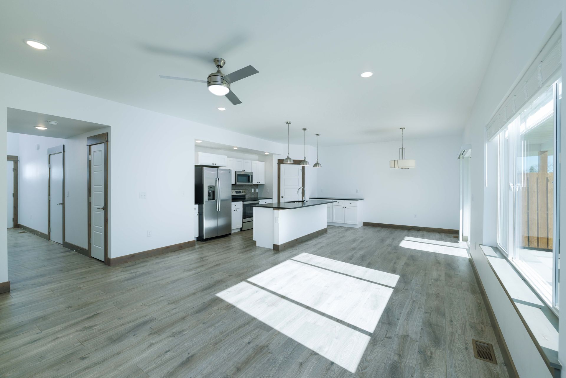 A living room with a ceiling fan and a kitchen in the background.