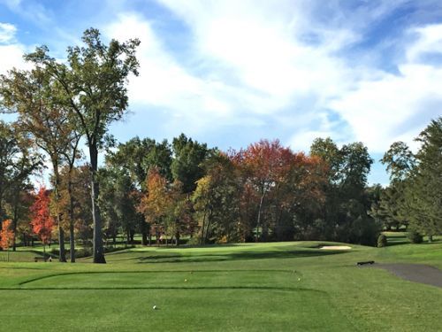 Golf course with colorful fall foliage and blue sky.