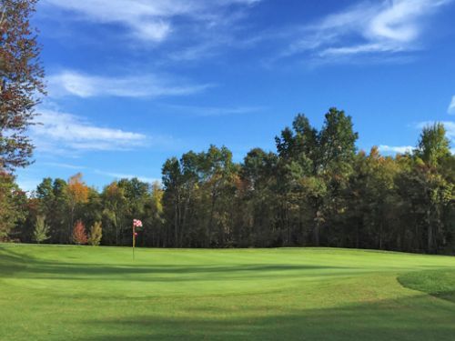 Green golf course with trees in fall colors under a blue sky, flag on the green.