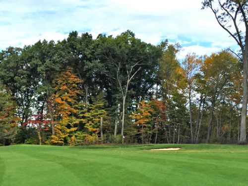 Green golf course with trees showing fall colors in the background.