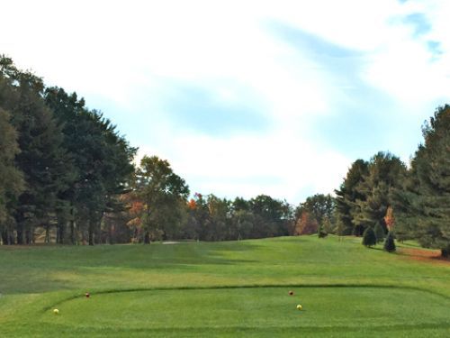 Golf course fairway with green grass, trees, and cloudy sky.