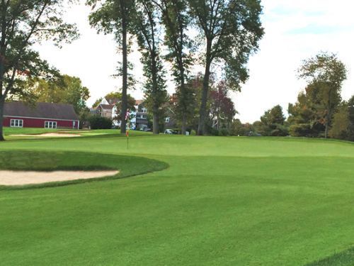 Green golf course with sand trap, trees, and buildings in the background.
