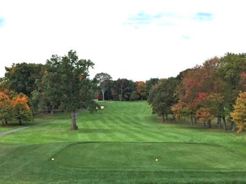 Golf course fairway with green grass, autumn trees, and a tee box.