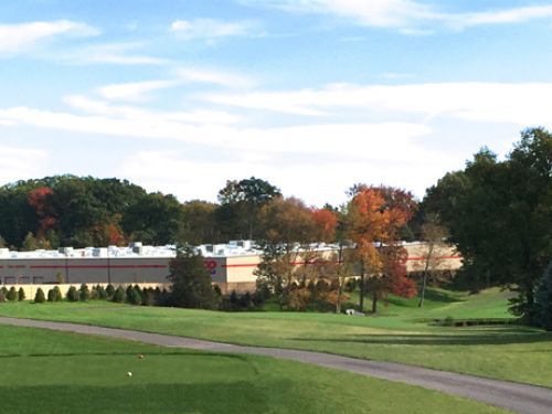 Golf course with a large commercial building in the background. Trees with autumn leaves dot the landscape.