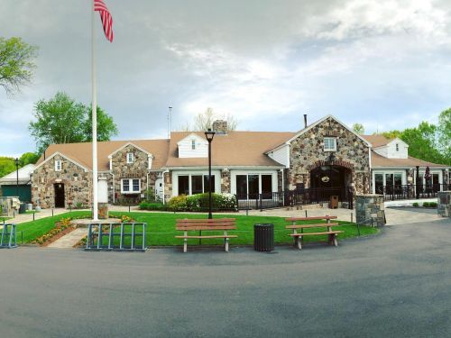 Stone building with US flag, green lawn, picnic tables, and a paved drive.